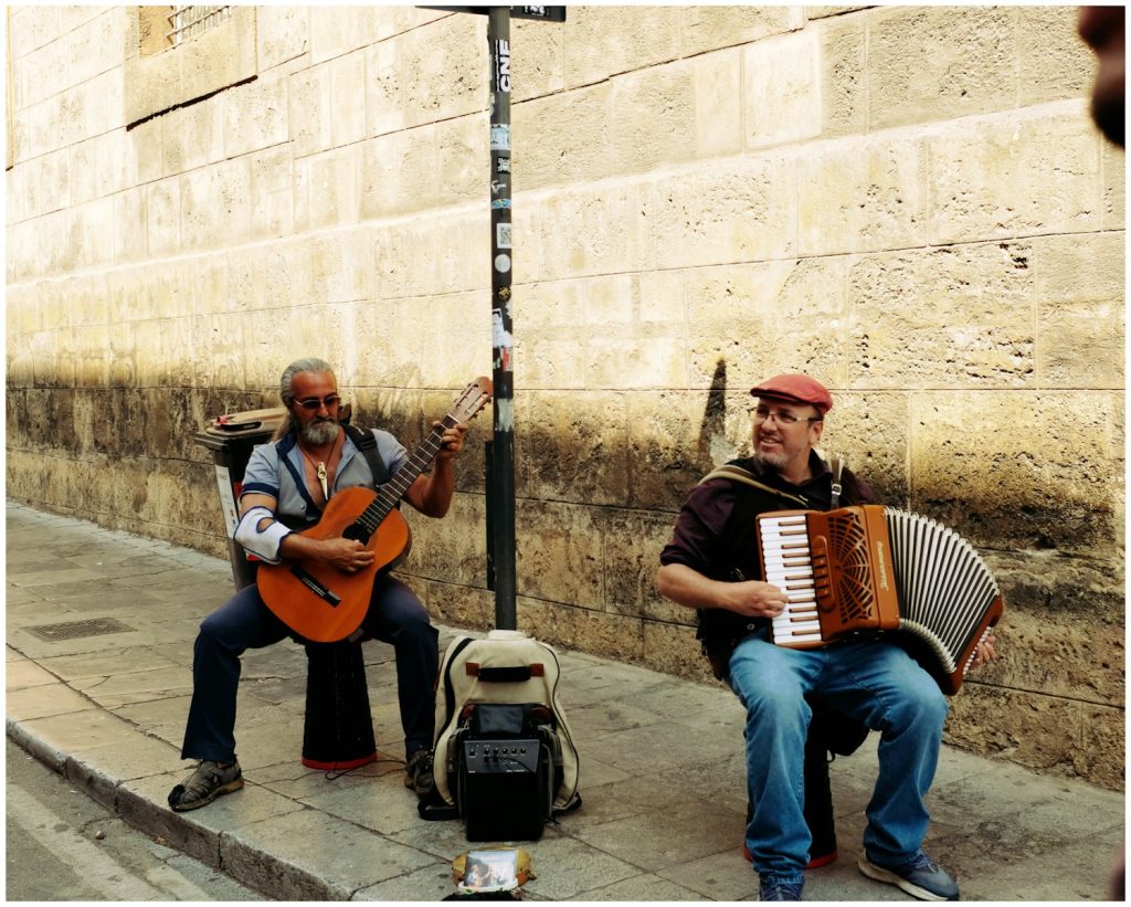 Two musicians play guitar and accordion on street.